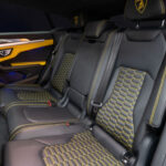 A white Lamborghini Urus with black and yellow interior, parked indoors, highlighting its sporty and luxurious design.