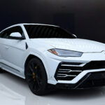 A white Lamborghini Urus with black and yellow interior, parked indoors, highlighting its sporty and luxurious design.