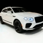 A white Bentley Bentayga with red interior seats, parked indoors, showcasing its luxurious and stylish design.