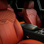 A white Bentley Bentayga with red interior seats, parked indoors, showcasing its luxurious and stylish design.
