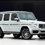 White Mercedes-Benz G63 AMG parked inside a warehouse with glossy white epoxy flooring and dark black walls.