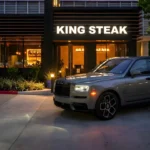 Grey Rolls-Royce Cullinan Black Badge rental parked in front of King Steak in the Houston Galleria area at dusk.
