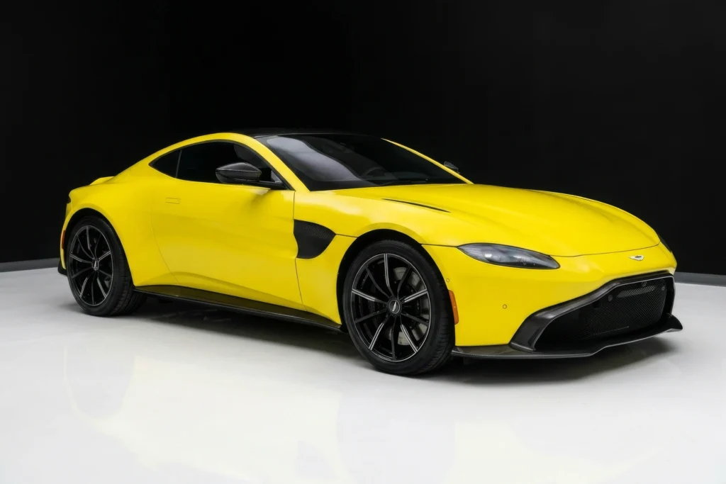 Front angle view of a yellow Aston Martin Vantage exotic rental car parked in a studio setting.